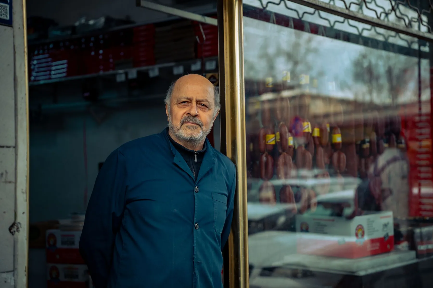Il titolare di un negozio sulla soglia della sua bottega, in camicia blu